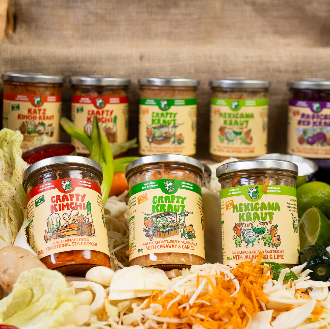 Three jars of sauerkraut and kimchi in front of shredded vegetables