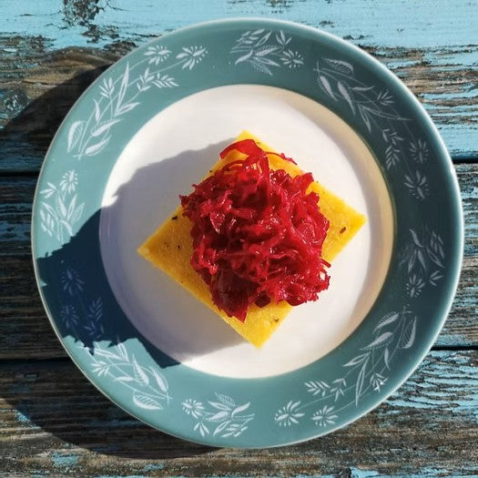 A blue and white plate with polenta cheese and reclaimed red kraut on top