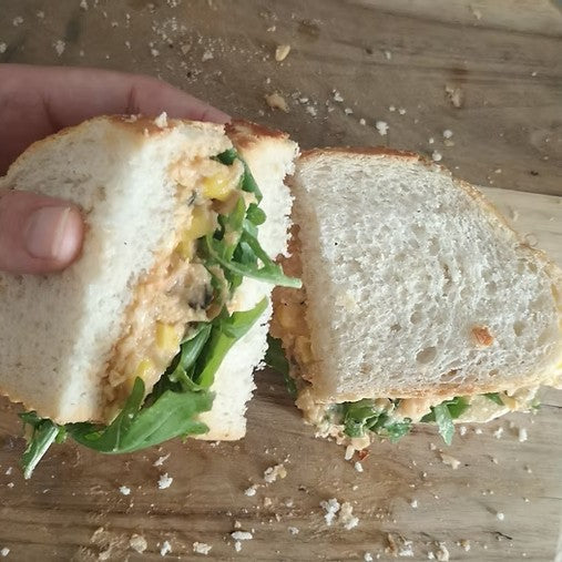 A chickpea chuna sandwhich with crafty kraut and lettece in a tiger bread sandwhich cut in half