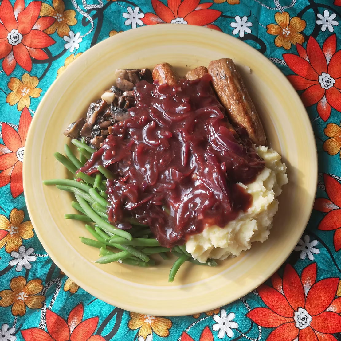 A plate of green beans mushrooms sausages and mash potato covered in reclaimed red kraut and onion gravy