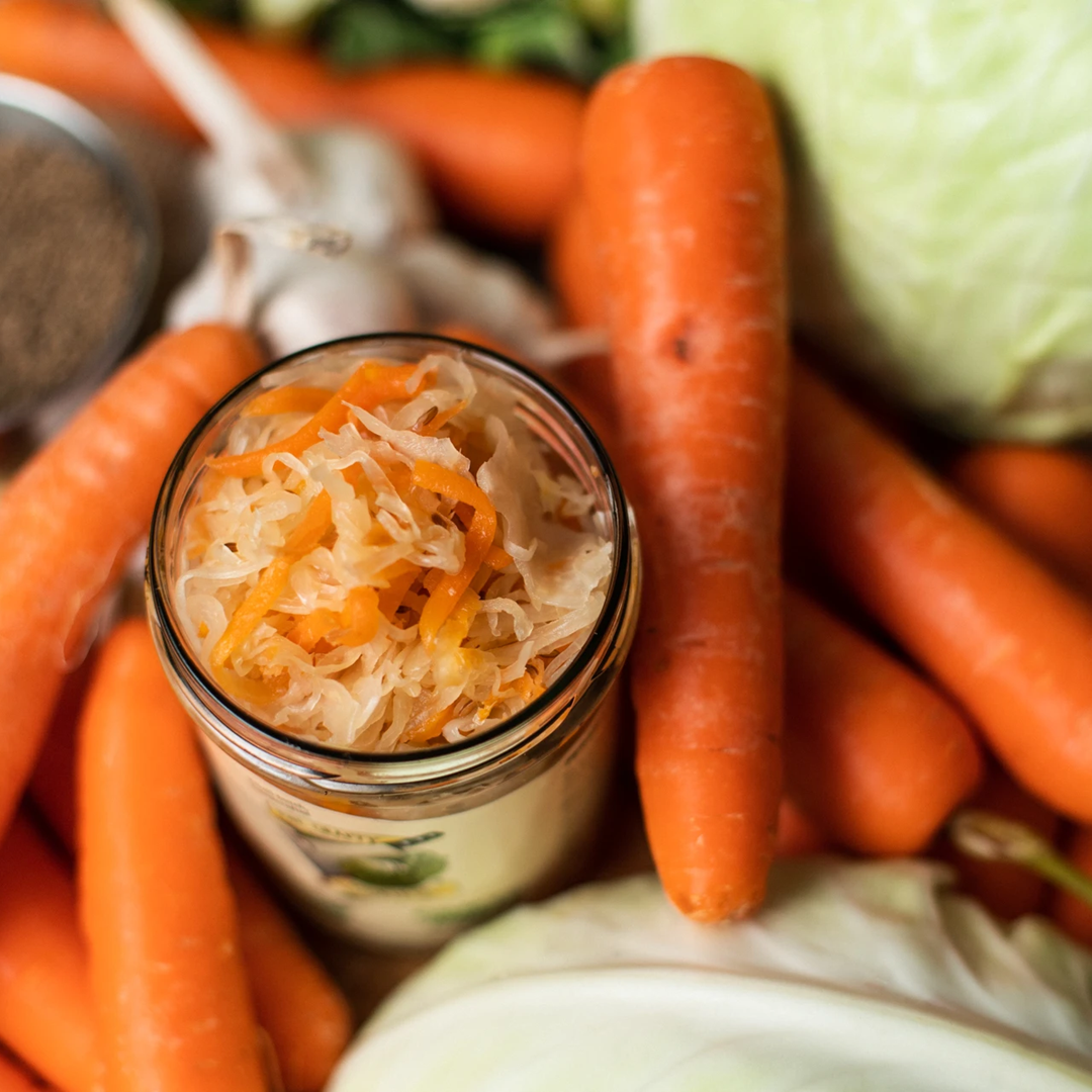 An open jar of crafty kraut surrounded by its fresh ingredients of cabbage and carrots