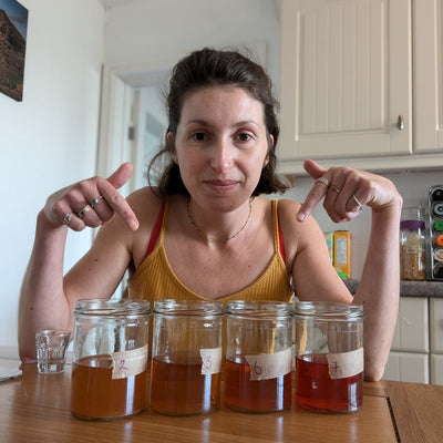 Madi pointing at 4 labelled glass jars of kombucha