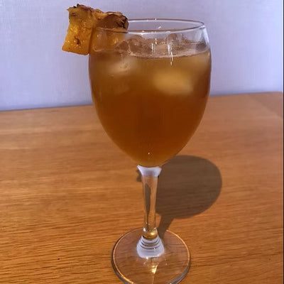A wine glass of tepache garnished with pineapple