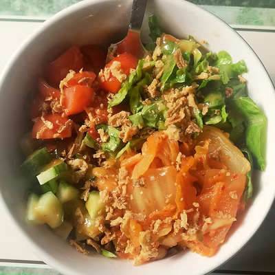 A salad bowl of lettece tomatoe cucumber and kimchi 
