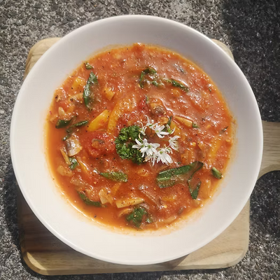 A bowl of spicy kimchi soups garnished with a wild garlic flower, on a wooden chopping board
