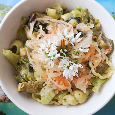 A bowl of pesto pasta with broccolli and veggie sausages, topped with crafty kraut