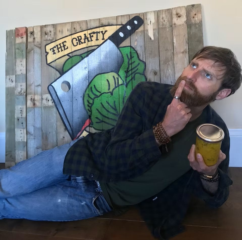 Crafty pickle Arthur with a jar of sauerkraut infront of crafty pickle sign