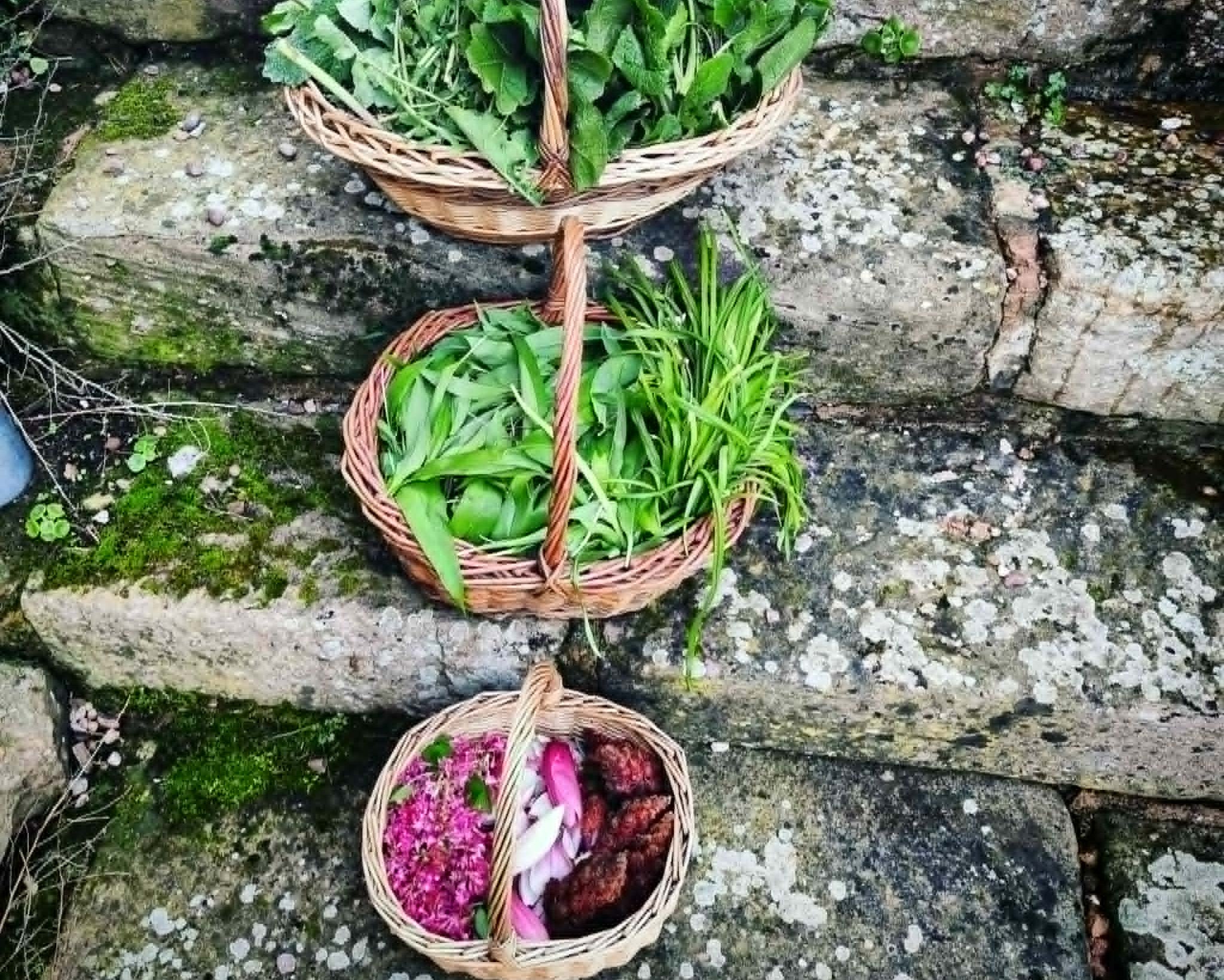Three woven baskets with fresh greens and flowers on a stone step