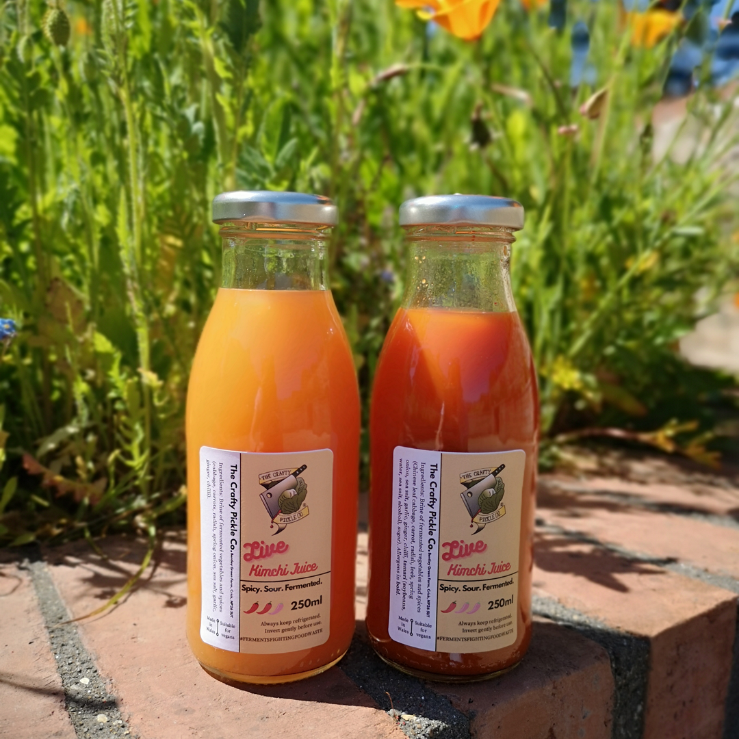 Two bottles of live hindo juice on a brick path with greenery in the background