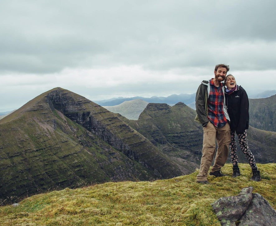 Two people standing on a mountain top with scenic views of the surrounding mountains.