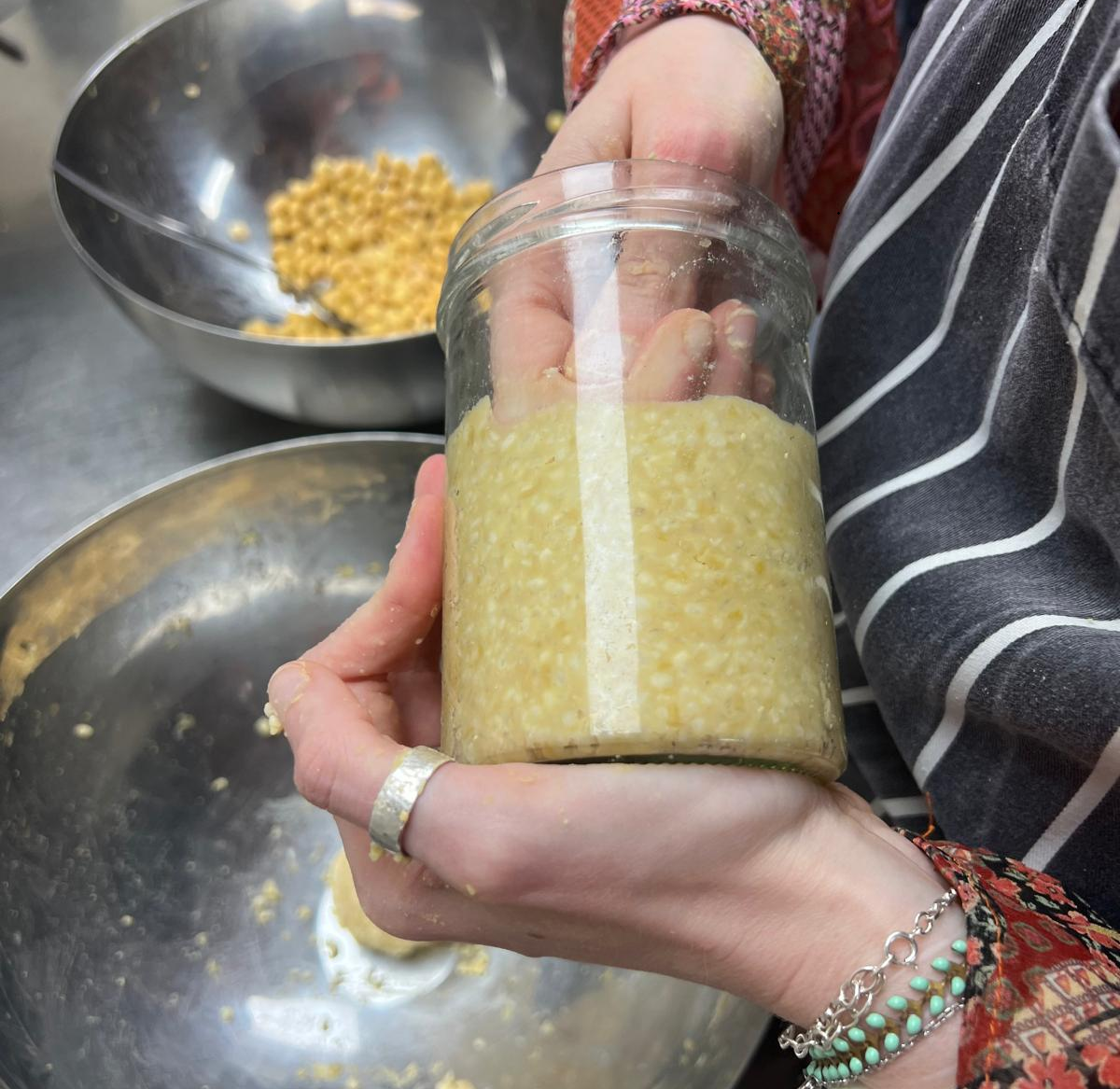 Hand holding a jar of miso with a bowl of soyabeans in the background.